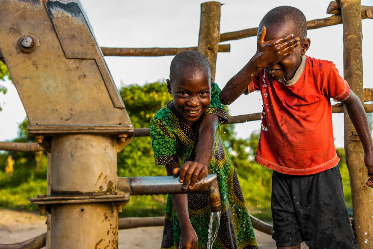 Two boys washing their face with water from charity: water well.